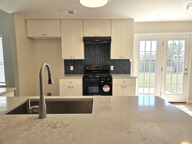 kitchen with visible vents, a sink, decorative backsplash, under cabinet range hood, and black range with gas stovetop