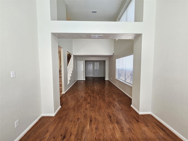 corridor featuring visible vents, baseboards, stairway, a towering ceiling, and dark wood-style floors