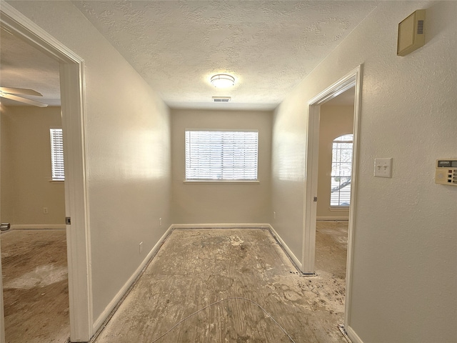 hallway featuring visible vents, baseboards, and a textured ceiling