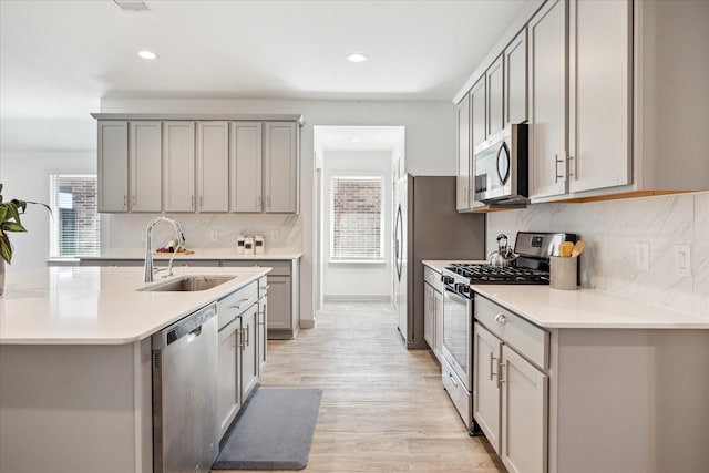 kitchen with gray cabinetry, light wood-type flooring, a wealth of natural light, stainless steel appliances, and a sink