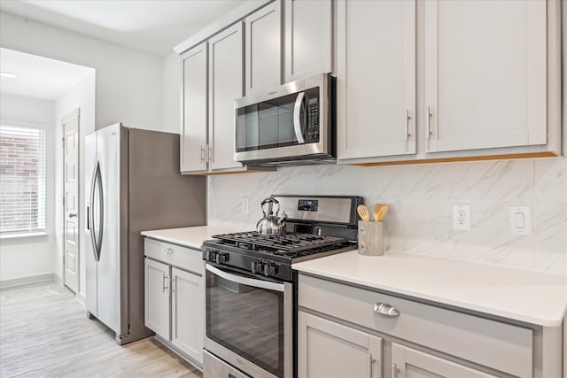 kitchen with stainless steel appliances, light wood finished floors, decorative backsplash, baseboards, and light countertops