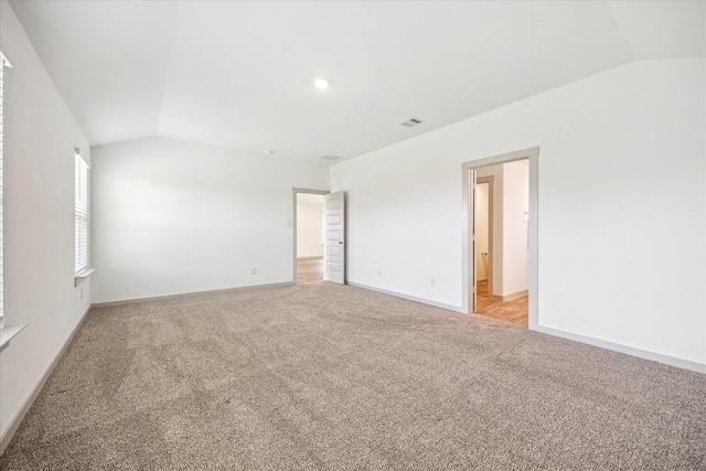 spare room with visible vents, light carpet, baseboards, and vaulted ceiling