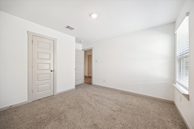 unfurnished bedroom with multiple windows, carpet, visible vents, and baseboards