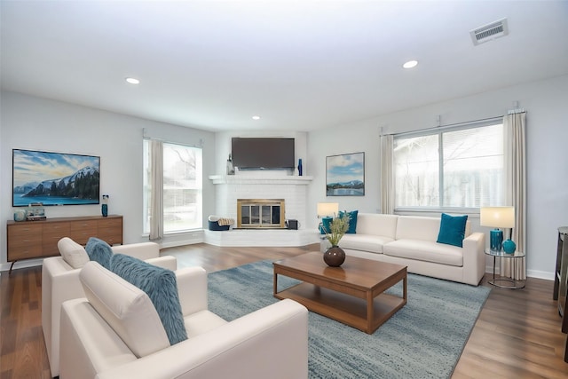 living room with visible vents, wood finished floors, recessed lighting, baseboards, and a brick fireplace