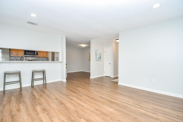 unfurnished living room with visible vents, baseboards, recessed lighting, light wood-style flooring, and a sink