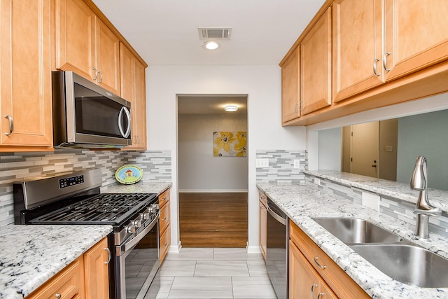 kitchen with visible vents, backsplash, light stone countertops, appliances with stainless steel finishes, and a sink