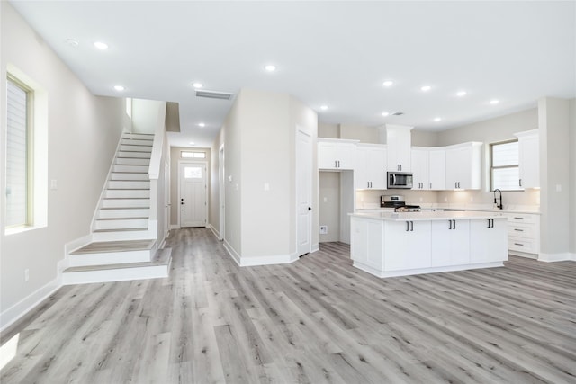 kitchen with a sink, stainless steel appliances, light countertops, white cabinets, and light wood-type flooring