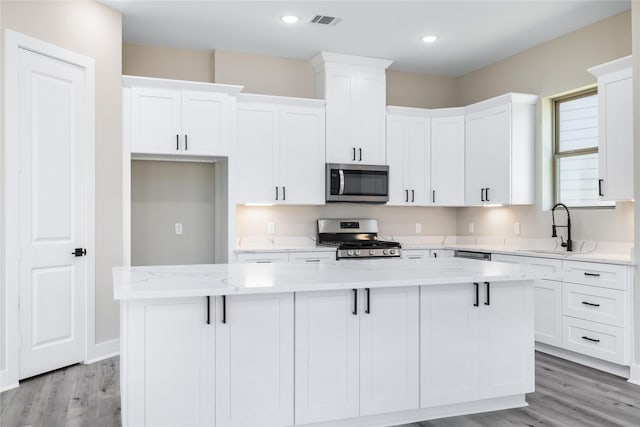 kitchen featuring visible vents, a kitchen island, white cabinets, stainless steel appliances, and a sink