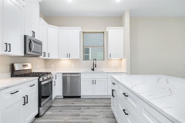 kitchen with light wood-style flooring, a sink, appliances with stainless steel finishes, white cabinets, and light stone countertops