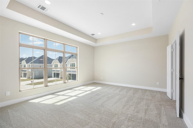 carpeted empty room featuring visible vents, a raised ceiling, and baseboards