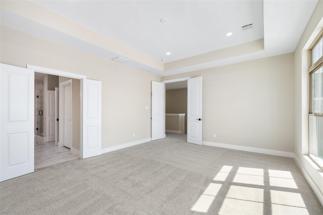 unfurnished bedroom with a tray ceiling, multiple windows, and light colored carpet