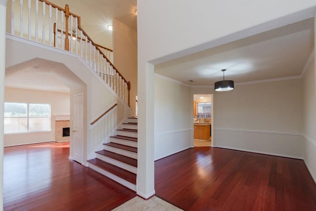 staircase with baseboards, ornamental molding, a fireplace, a towering ceiling, and wood finished floors