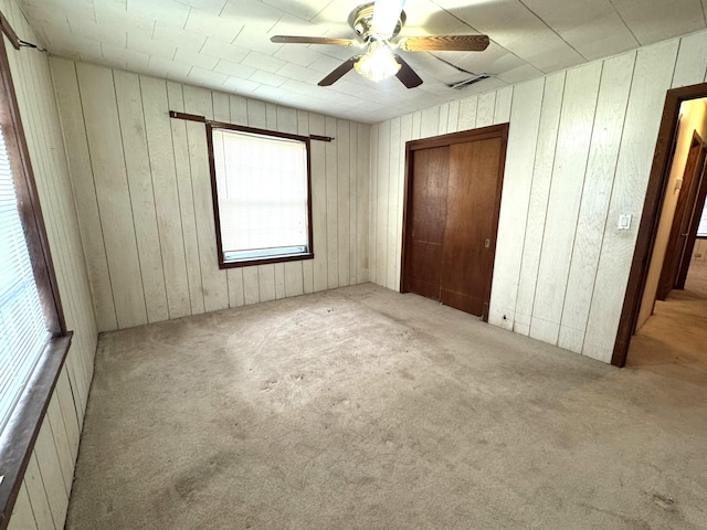 unfurnished bedroom with wooden walls, a ceiling fan, a closet, and carpet floors