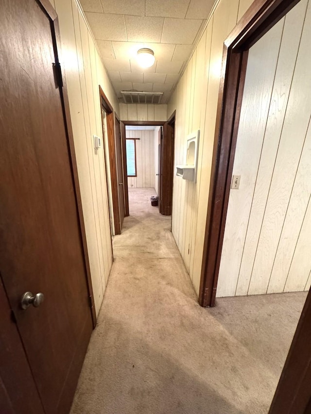 corridor featuring visible vents, wood walls, and light carpet