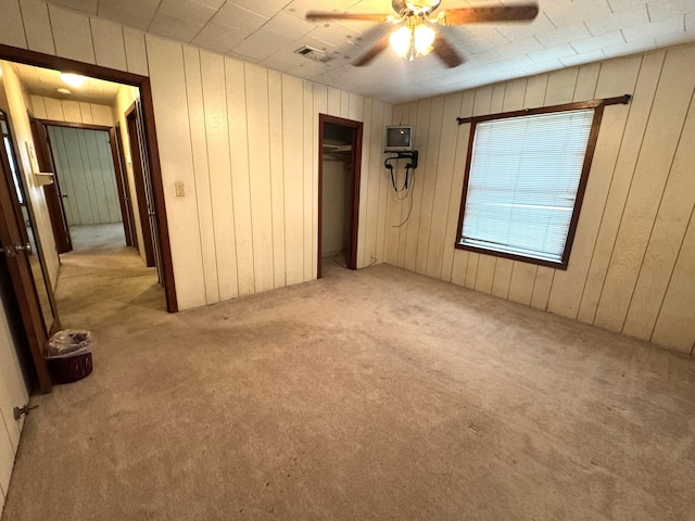 unfurnished bedroom with visible vents, light carpet, a ceiling fan, a closet, and wood walls