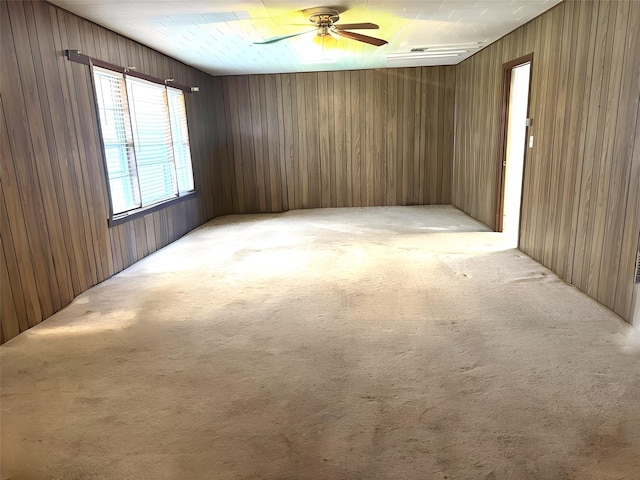 unfurnished room with light carpet, wood walls, and a ceiling fan