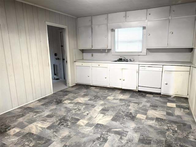 kitchen with wooden walls, dishwasher, light countertops, white cabinetry, and a sink