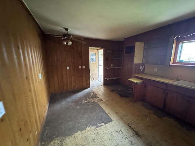 kitchen with wooden walls, light countertops, ceiling fan, and a sink