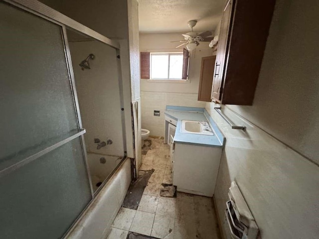 full bathroom with ceiling fan, bath / shower combo with glass door, toilet, vanity, and a textured ceiling