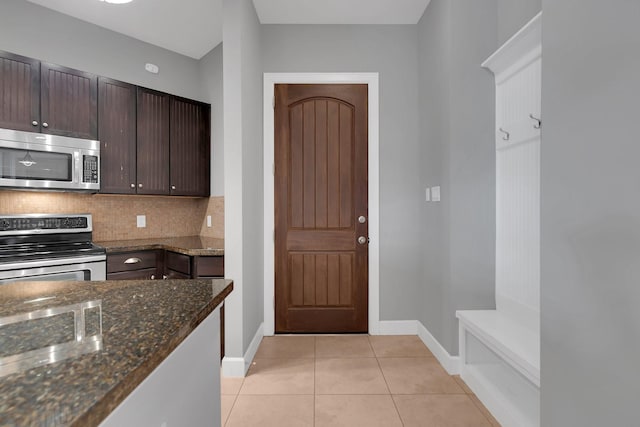 kitchen with dark stone counters, light tile patterned flooring, stainless steel appliances, dark brown cabinets, and backsplash