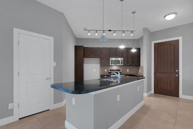 kitchen featuring dark countertops, stainless steel microwave, dark brown cabinets, decorative backsplash, and a sink