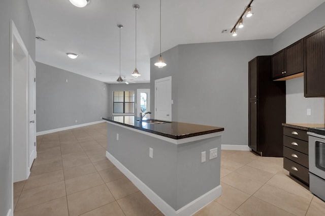 kitchen featuring dark countertops, a sink, dark brown cabinets, light tile patterned floors, and a kitchen island with sink