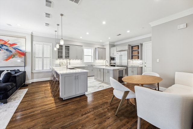 kitchen with visible vents, built in appliances, a kitchen island with sink, and gray cabinets