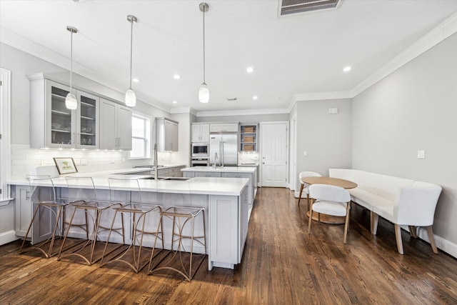 kitchen featuring visible vents, a peninsula, built in appliances, a kitchen bar, and tasteful backsplash