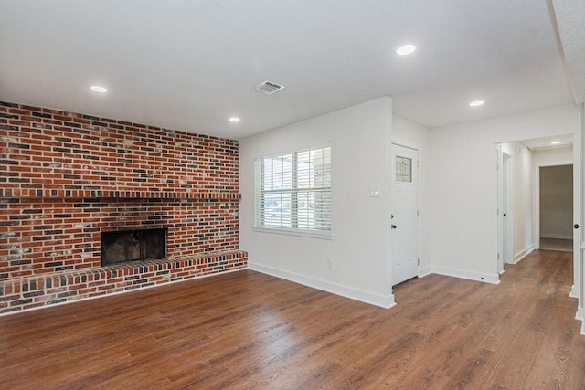 unfurnished living room featuring wood finished floors, visible vents, baseboards, recessed lighting, and a brick fireplace