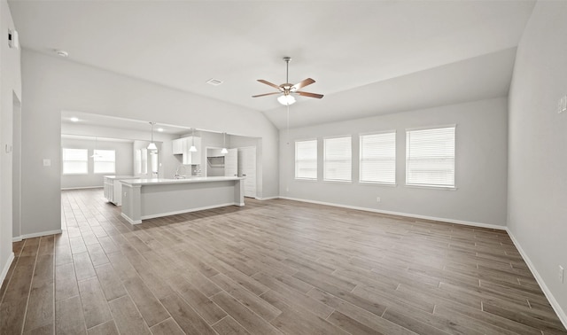 unfurnished living room featuring a sink, a ceiling fan, lofted ceiling, and wood finished floors