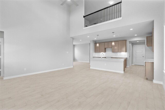 357 Spruce Oak Ln, Waller, TX 77484 - unfurnished living room with a sink, ceiling fan, light wood-type flooring, a towering ceiling, and baseboards