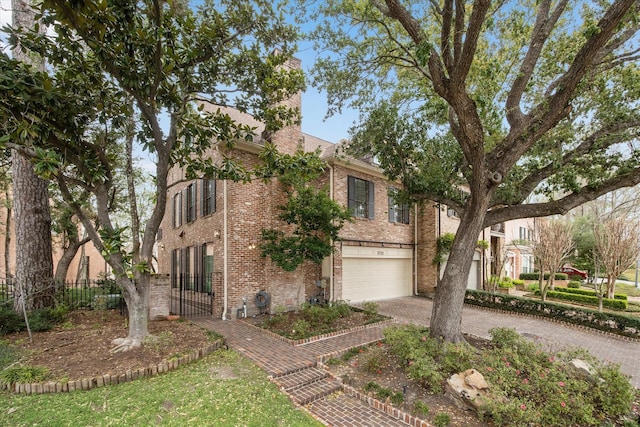 view of front of house with brick siding, an attached garage, fence, a chimney, and driveway