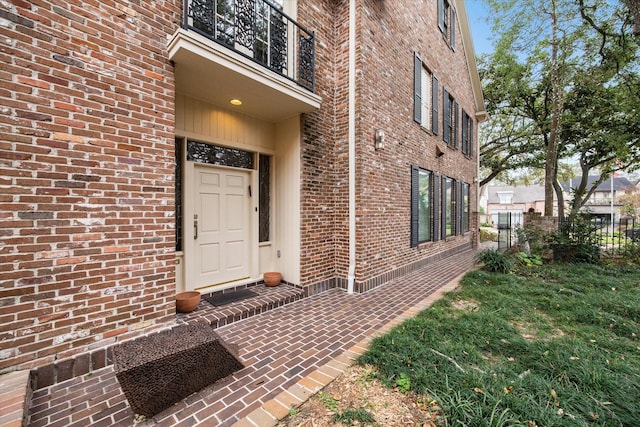 view of exterior entry with brick siding, a balcony, and fence