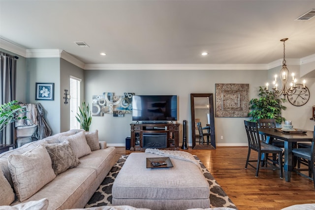 living area featuring visible vents, crown molding, baseboards, a chandelier, and wood finished floors