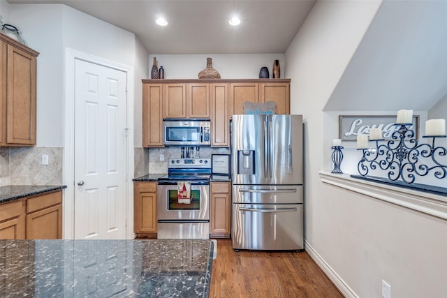 kitchen featuring backsplash, baseboards, dark stone counters, wood finished floors, and stainless steel appliances