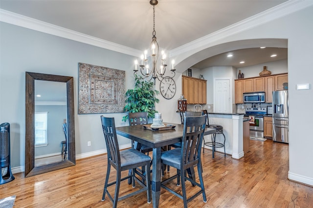 dining space featuring crown molding, baseboards, arched walkways, and light wood finished floors