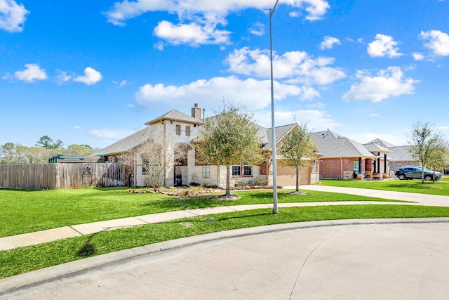 french country inspired facade featuring a front yard, fence, an attached garage, concrete driveway, and stone siding