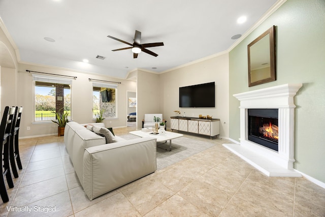 living room with baseboards, a ceiling fan, a warm lit fireplace, and crown molding