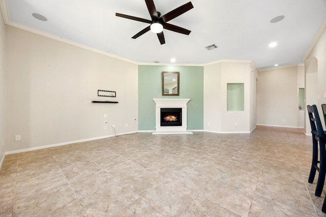 unfurnished living room with baseboards, visible vents, ornamental molding, a lit fireplace, and ceiling fan