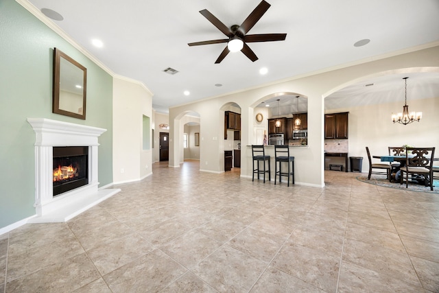 living room with visible vents, baseboards, ornamental molding, ceiling fan with notable chandelier, and a glass covered fireplace