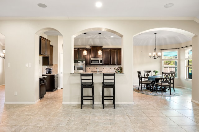 kitchen with a breakfast bar, dark brown cabinets, appliances with stainless steel finishes, a notable chandelier, and backsplash