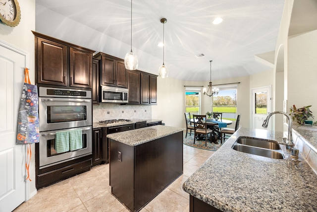 kitchen featuring a sink, backsplash, a kitchen island, stainless steel appliances, and light stone countertops