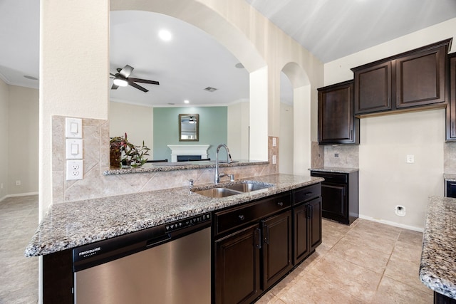 kitchen featuring a ceiling fan, a sink, stainless steel dishwasher, arched walkways, and a fireplace