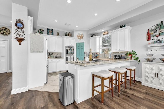 kitchen with stainless steel double oven, wood finished floors, a peninsula, and white cabinets