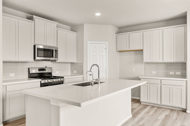 kitchen with light wood-style flooring, a center island with sink, a sink, backsplash, and stainless steel appliances