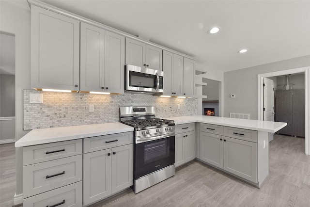 kitchen featuring visible vents, light wood finished floors, a peninsula, stainless steel appliances, and decorative backsplash