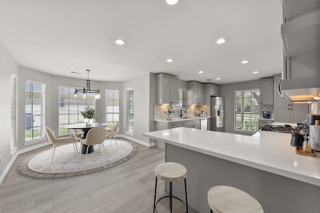 kitchen with light countertops, decorative backsplash, gray cabinets, a peninsula, and stainless steel refrigerator with ice dispenser