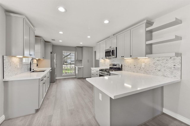 kitchen with gray cabinets, a sink, light countertops, appliances with stainless steel finishes, and light wood-type flooring