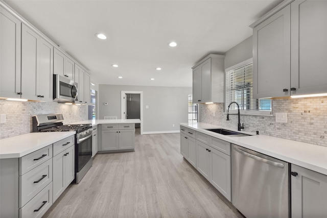 kitchen with light wood-style flooring, gray cabinets, stainless steel appliances, and a sink