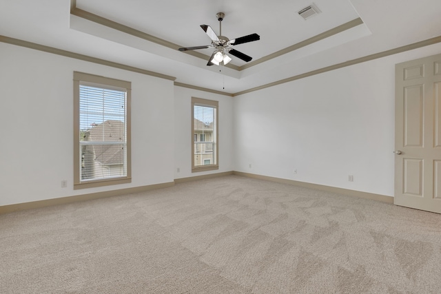 spare room with a tray ceiling, light colored carpet, visible vents, and crown molding